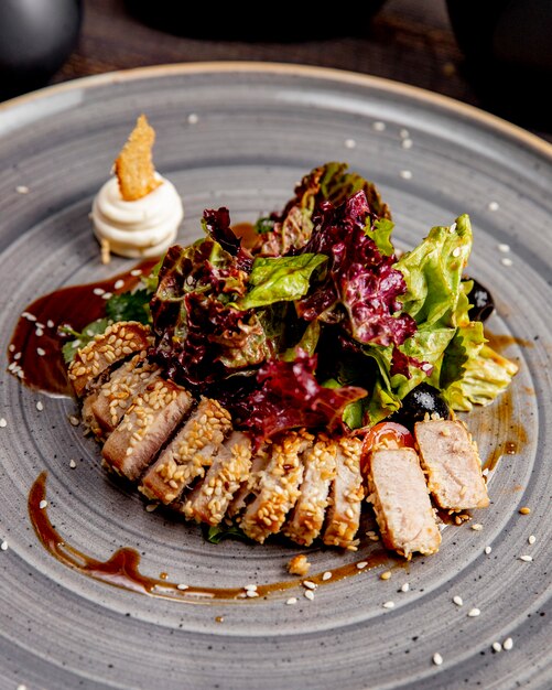 Slices of meat served with lettuce sesame seeds and sauce