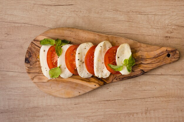 Slices of mozzarella cheese; tomatoes with herb on chopping board against wooden backdrop