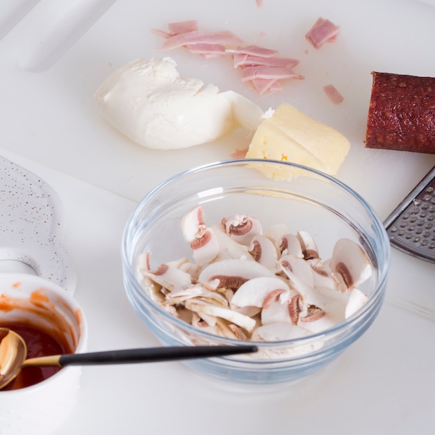 Free photo slices of mushroom; cheese; butter; ham; sauce and salami on chopping board