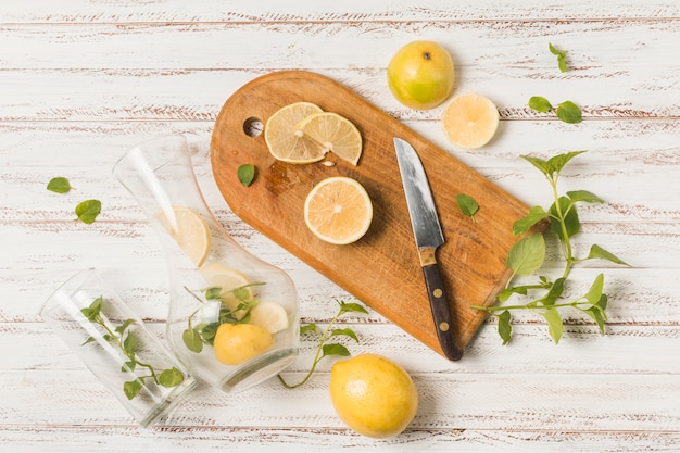 Бесплатное фото Ломтики фруктов возле ножа на разделочной доске между травами и стаканами