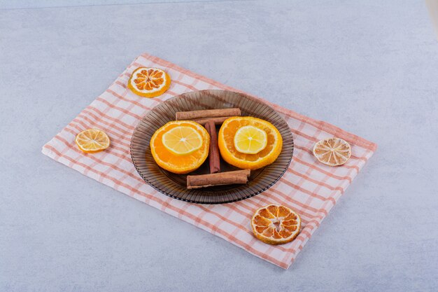 Ломтики апельсина и лимона в стеклянной миске с палочками корицы.