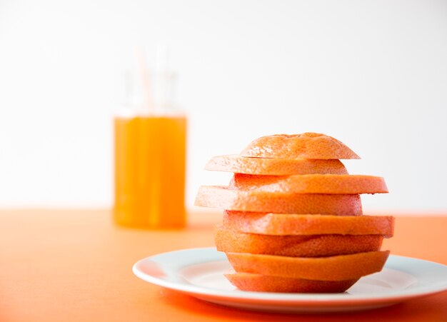 Slices of orange stacked over one another on white plate in front of juice bottle