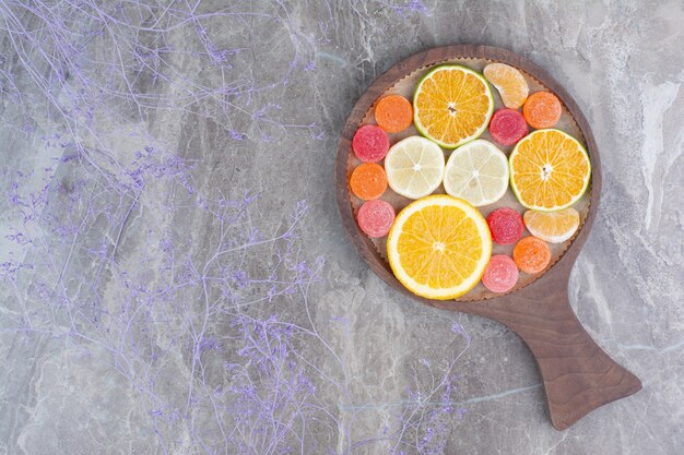 Slices of orange, tangerine and candies on cutting board. 