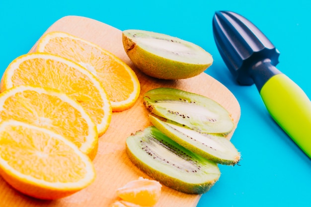 Slices of oranges and kiwi slices and hand juicer on blue background