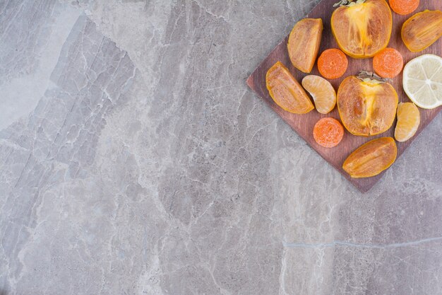 Slices of persimmon, lemon, tangerine and candies on board. 