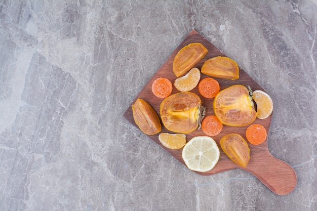 Foto gratuita fette di cachi, limone, mandarino e caramelle a bordo.