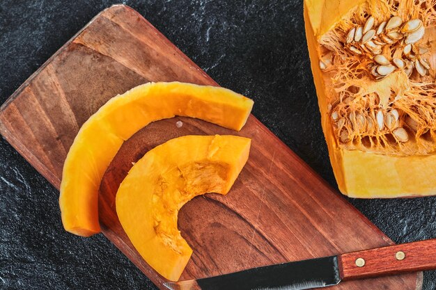 Slices of pumpkin on wooden chopping board with knife.