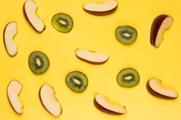 Free photo slices of ripe red apples and juicy kiwi on yellow background