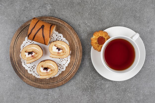 Slices of sweet roll cake on wooden board with cup of tea