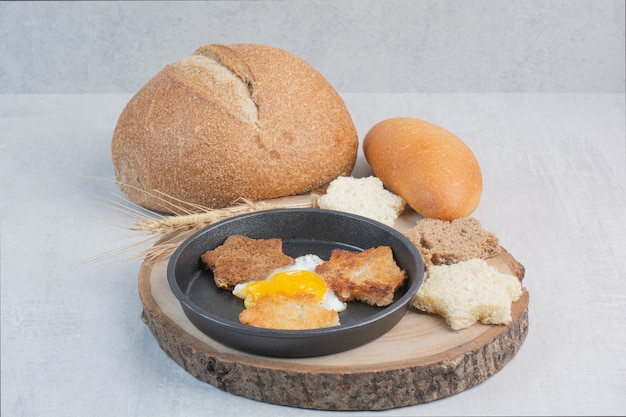Кусочки белого и черного хлеба с жареным яйцом на деревянной тарелке.