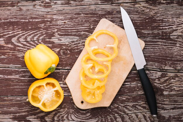 Slices of yellow bell pepper on chopping board with knife against wooden desk