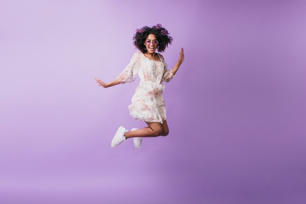 점프 하 고 웃 고 흰색 운동 화에 슬림 아프리카 여자. 기분 좋은 흑인 소녀 춤의 실내 사진.