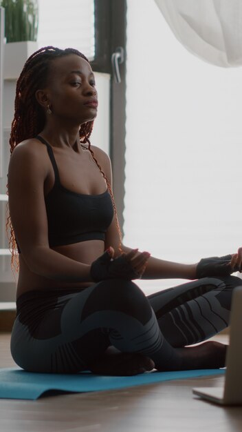 Slim black woman sitting in lotus pose on yoga map with closed eyes