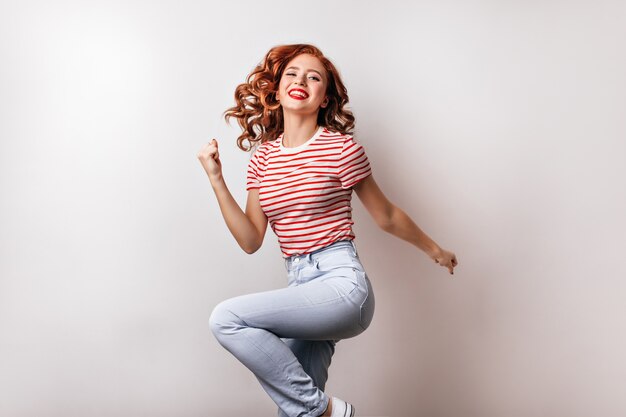 Slim cute woman in jeans dancing . Debonair smiling girl jumping on white wall.