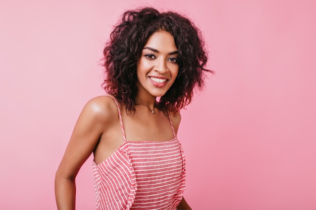 Slim dark-eyed African female model smiles sweetly. Portrait of girl in stylish outfit and beautiful jewelry on neck.