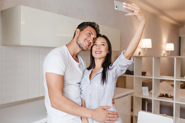 Slim dark-haired woman making selfie with husband before breakfast