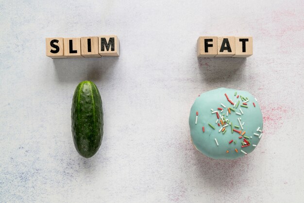Slim; fat text on wooden blocks with cucumber and glazed donut over rough backdrop