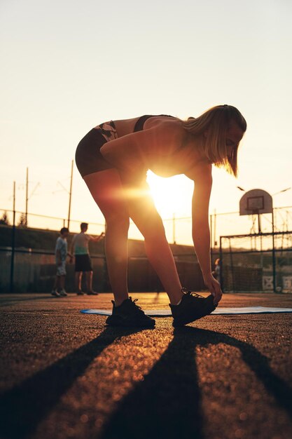 スポーツフィールドでストレッチストレッチのスリムな女性