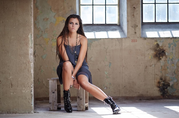 Slim female with long brown hair in sexy blue dress posing on wooden chair.