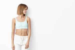 Free photo slim fitness young female wearing white top and trousers, isolated, going in gym to have sport training, preparing for competition, looking aside with thoughtful expression