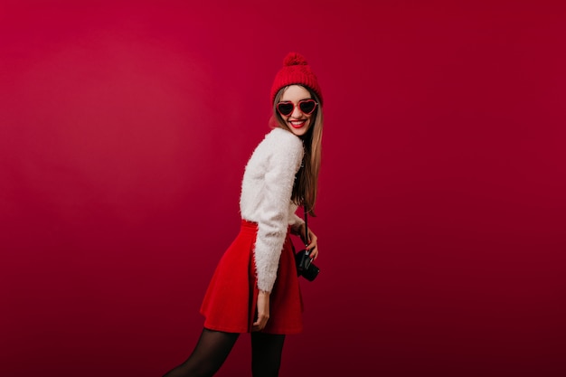 Slim girl in knitted hat posing with camera and smiling