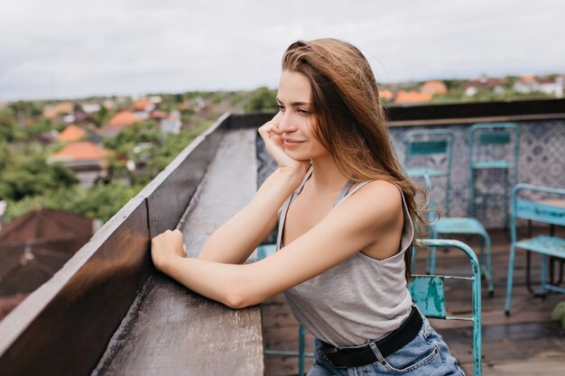 Slim girl wears black belt relaxing at roof in spring morning. Outdoor portrait of glad european woman looking at sky with smile.