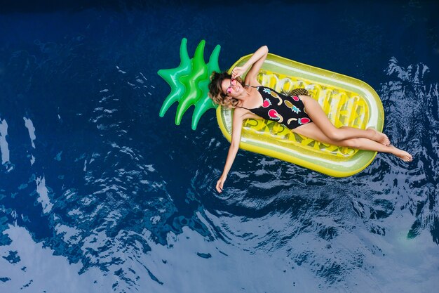 Slim girl with tanned skin laughing while lying on mattress at sea resort. Outdoor photo of good-looking female model in sparkle sunglasses.