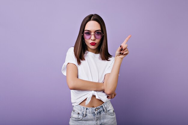 Slim glamorous lady posing with serious face expression. Indoor portrait of beautiful brunette girl standing.