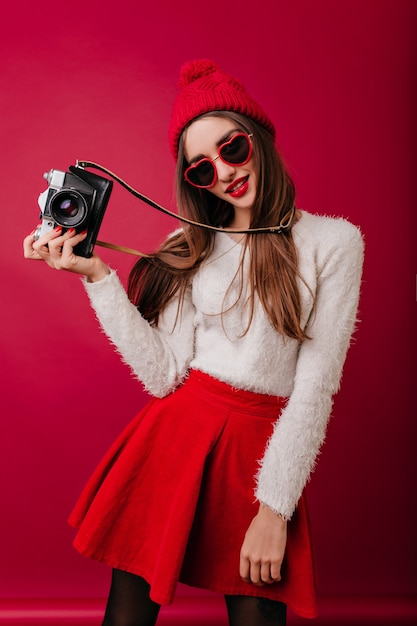 Slim gorgeous woman in red hat and skirt posing with camera