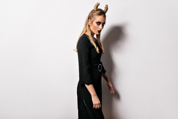 ハロウィーンの衣装でスリムな真面目な女性パーティーの準備をしている黒いドレスの夢のような女性モデル。