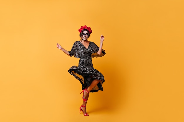Slim tanned mexican woman with crown of flowers jumps and dances  with orange walls