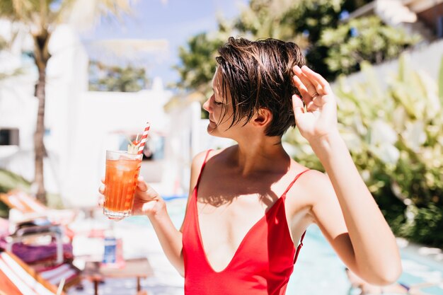 Стройная белая девушка позирует с бокалом коктейля на курорте.