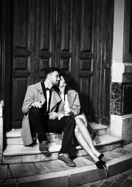 Стройная женщина целует молодого счастливого человека и сидит возле двери на улице