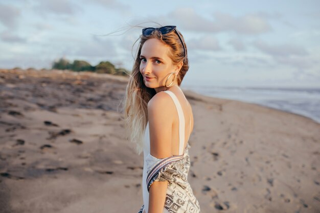 Slim woman with light-brown hair posing with smile at beach.