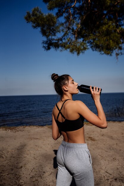 Slim young woman drinking water after training