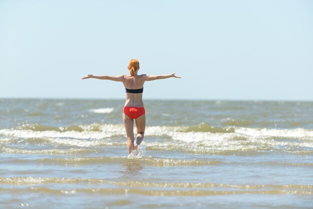 Slim young woman running into sea waves