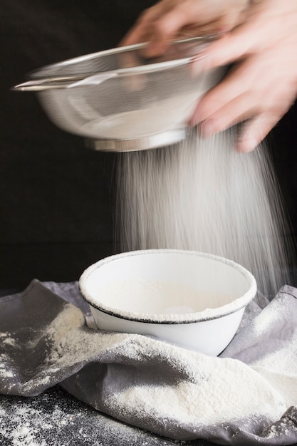 Slow motion shot of aged female hands sifting flour by sieve in bowl