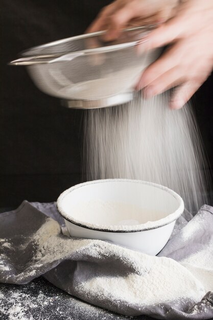 ボウルにふるいで小麦粉をふるいにかける高齢者の女性の手のスローモーション撮影