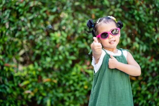 Маленькая азиатская девочка позирует в парке в солнечных очках