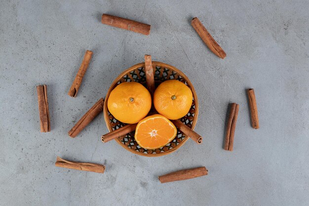 Small basket of oranges with cinnamon cuts on marble table.