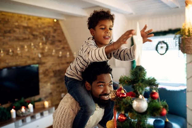 父親と一緒にクリスマスツリーを飾り、星を上に置く小さな黒い男の子