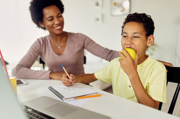 Small black boy eating an apple while doing homework