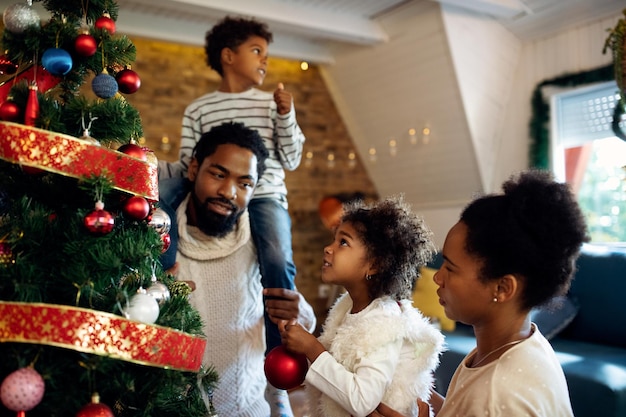 Small black girl and her family decorating Christmas tree at home