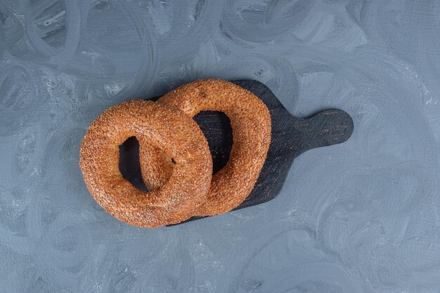 Small board with two bagels on top on marble table.