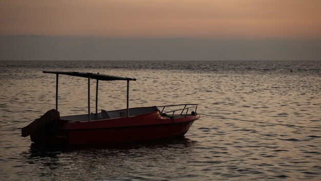 Small boat floats on the water with  mountains. 