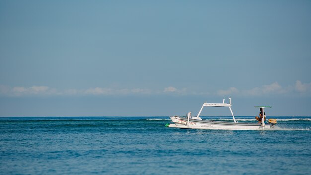 Small boat floats on the water with mountains. 