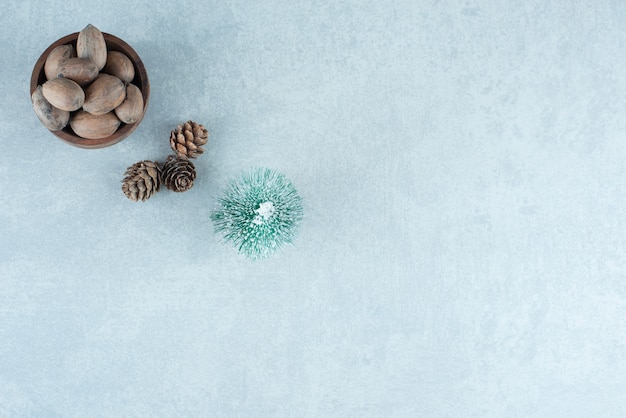 Small bowl of almonds, pine cones and a tree figurine on marble.