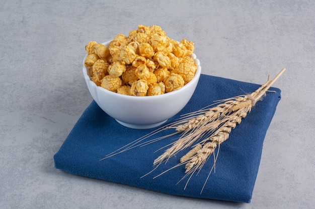 Small bowl of candy coated popcorn and stalks of wheat on marble.