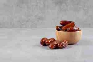 Free photo a small bowl of dates next to a handful on marble background. high quality photo