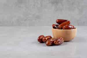 Free photo a small bowl of dates next to a handful on marble background. high quality photo